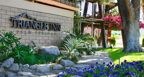 Blue flowers are planted in front of the welcoming Triangle Inn Palm Springs sign at the entrance to this men's clothing-optional resort