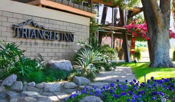 Blue flowers are planted in front of the welcoming Triangle Inn Palm Springs sign at the entrance to this men's clothing-optional resort