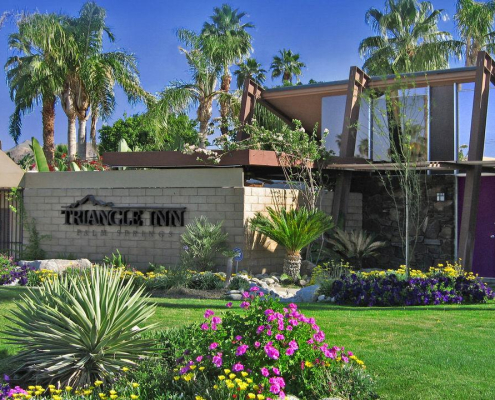 The front entrance of the Triangle Inn men's clothing-optional boutique hotel in Palm Springs, California, has purple and yellow and pink flowers and green grass