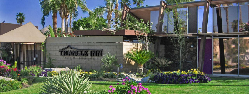 The front entrance of the Triangle Inn men's clothing-optional boutique hotel in Palm Springs, California, has purple and yellow and pink flowers and green grass