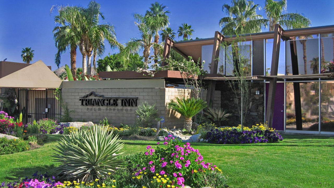 The front entrance of the Triangle Inn men's clothing-optional boutique hotel in Palm Springs, California, has purple and yellow and pink flowers and green grass