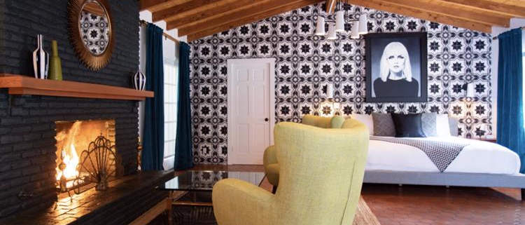 A chair and fireplace in a room at Villa Royale Palm Springs that has a tile wall and hanging picture of Debbie Harry