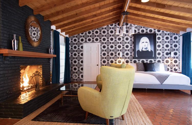 A chair and fireplace in a room at Villa Royale Palm Springs that has a tile wall and hanging picture of Debbie Harry