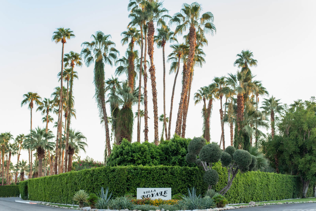 Villa Royale Hotel exterior sign with a hedge and palm trees behind it