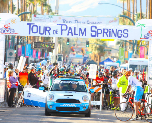 A sign reading "Tour de Palm Springs" with a car and people underneath it