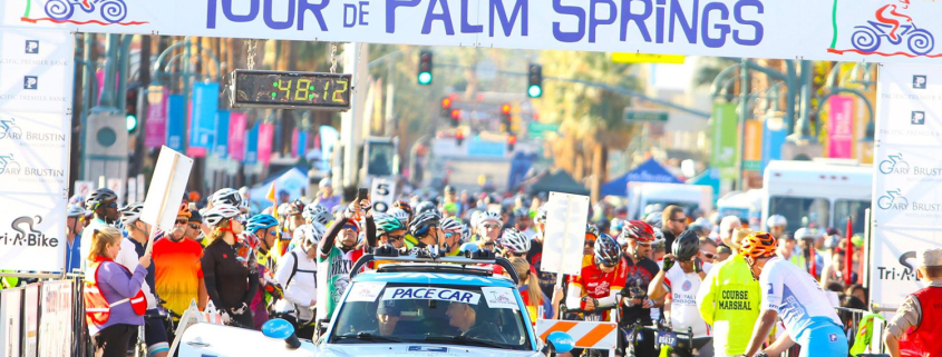 A sign reading "Tour de Palm Springs" with a car and people underneath it