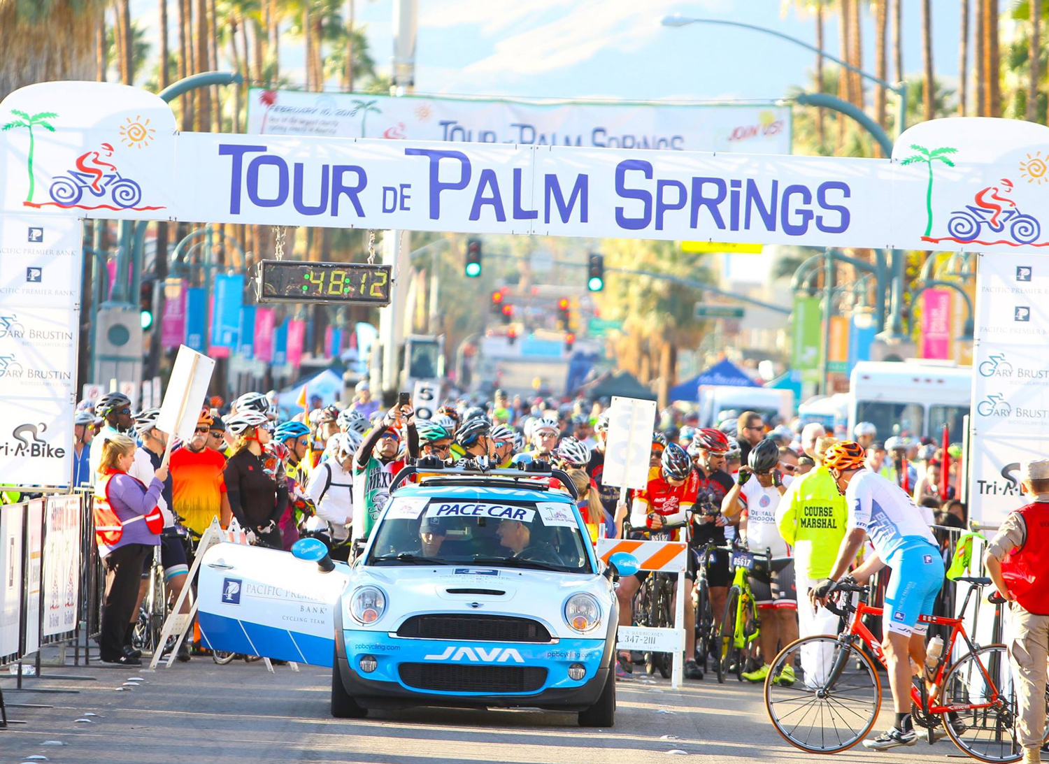 A sign reading "Tour de Palm Springs" with a car and people underneath it