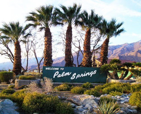 Palm trees flank the old Welcome to Palm Springs sign in Palm Springs, California