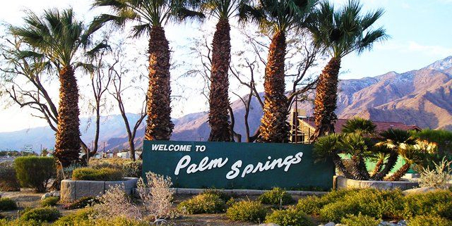 Palm trees flank the old Welcome to Palm Springs sign in Palm Springs, California