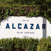 The white sign at the front of Alcazar Palm Springs with blue letters spelling out the hotel's name