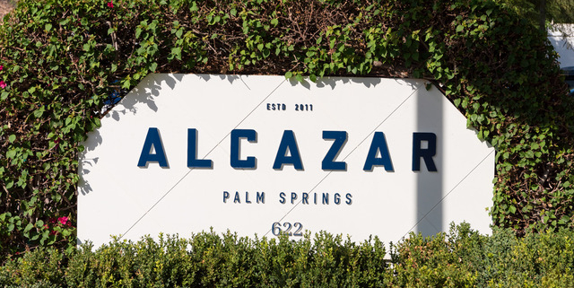 The white sign at the front of Alcazar Palm Springs with blue letters spelling out the hotel's name