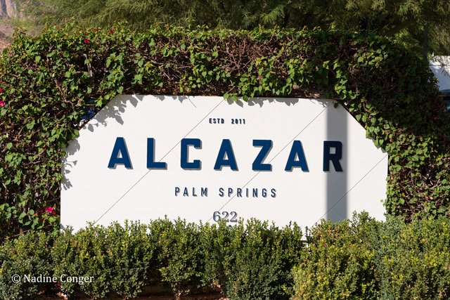 The white sign at the front of Alcazar Palm Springs with blue letters spelling out the hotel's name