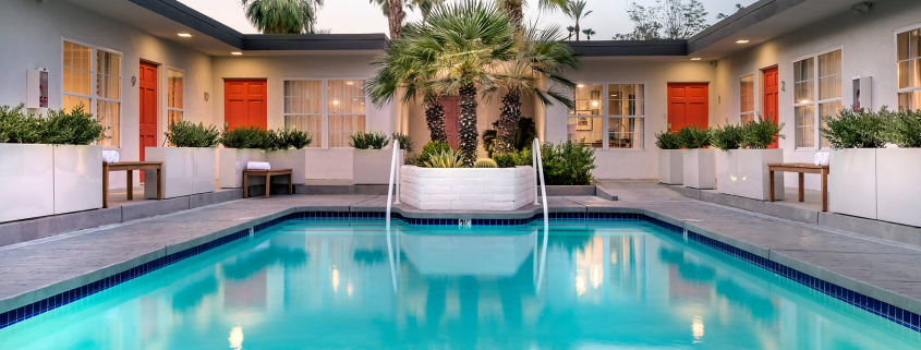 The courtyard pool at The Weekend Palm Springs surrounded by palm trees and the orange doors that lead to individual rooms