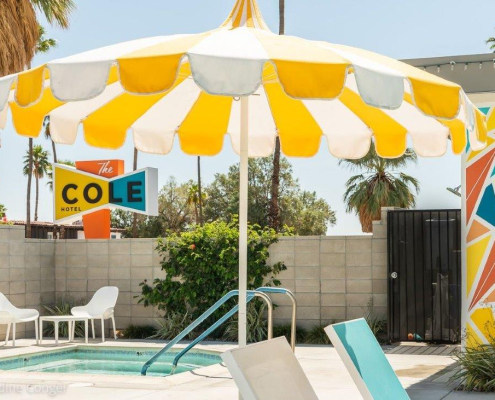 A fun yellow and white striped umbrella offers shade by the pool at The Cole Hotel in Palm Springs, California