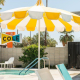 A fun yellow and white striped umbrella offers shade by the pool at The Cole Hotel in Palm Springs, California