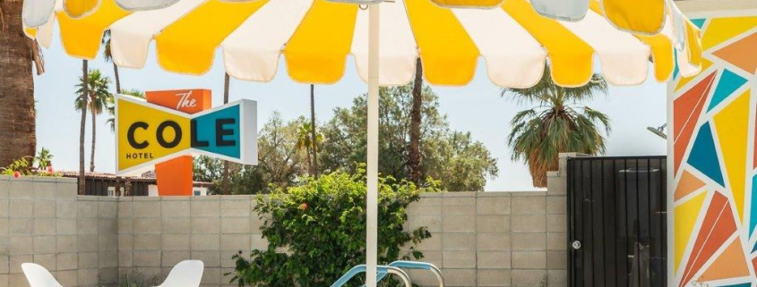 A fun yellow and white striped umbrella offers shade by the pool at The Cole Hotel in Palm Springs, California