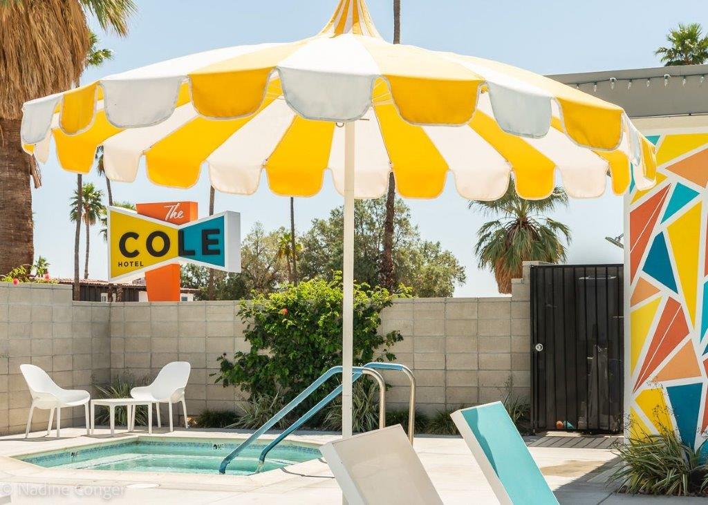 A fun yellow and white striped umbrella offers shade by the pool at The Cole Hotel in Palm Springs, California