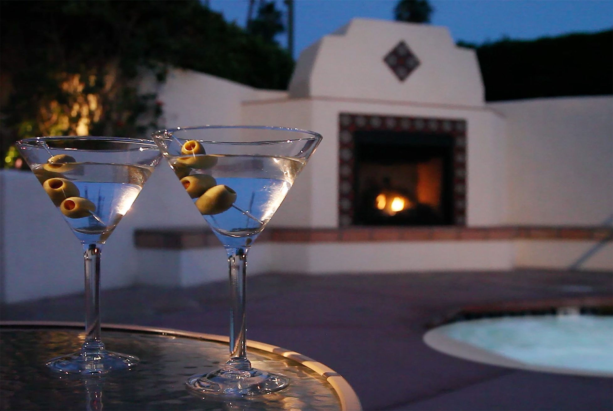 Two martini glasses on a table in front of a fireplace outside at the Hacienda at Warm Sands