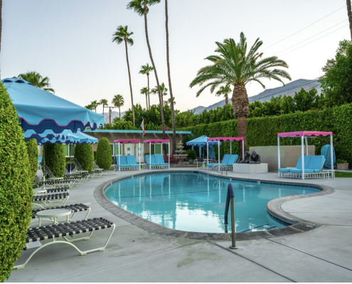 Pink and blue umbrellas and lounge chairs surround the relaxing pool at INNdulge Palm Springs men's clothing-optional resort in Palm Springs, California