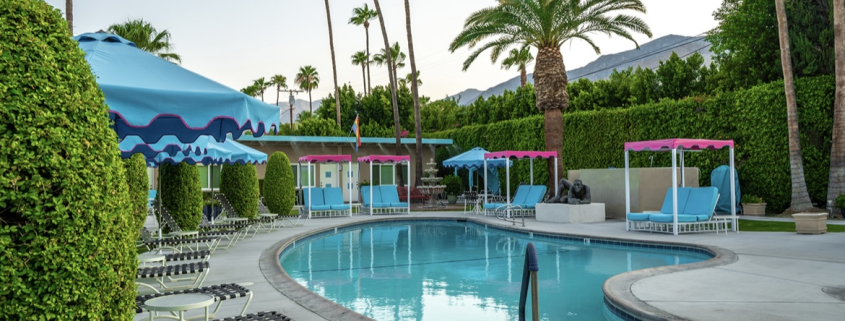 Pink and blue umbrellas and lounge chairs surround the relaxing pool at INNdulge Palm Springs men's clothing-optional resort in Palm Springs, California