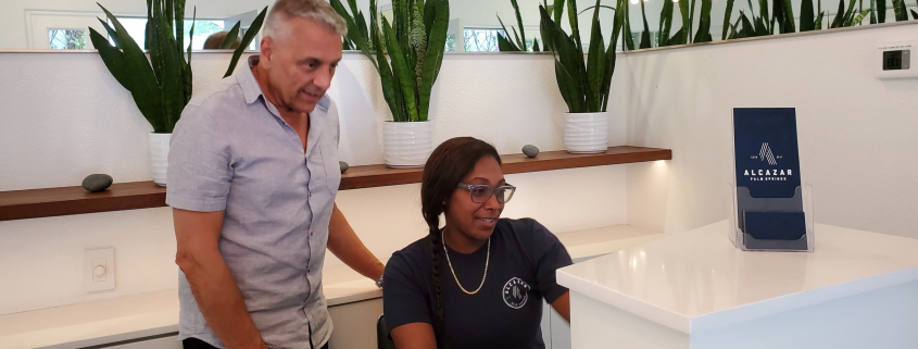 A man and a woman behind the front desk at Alcazar Palm Springs look at a computer