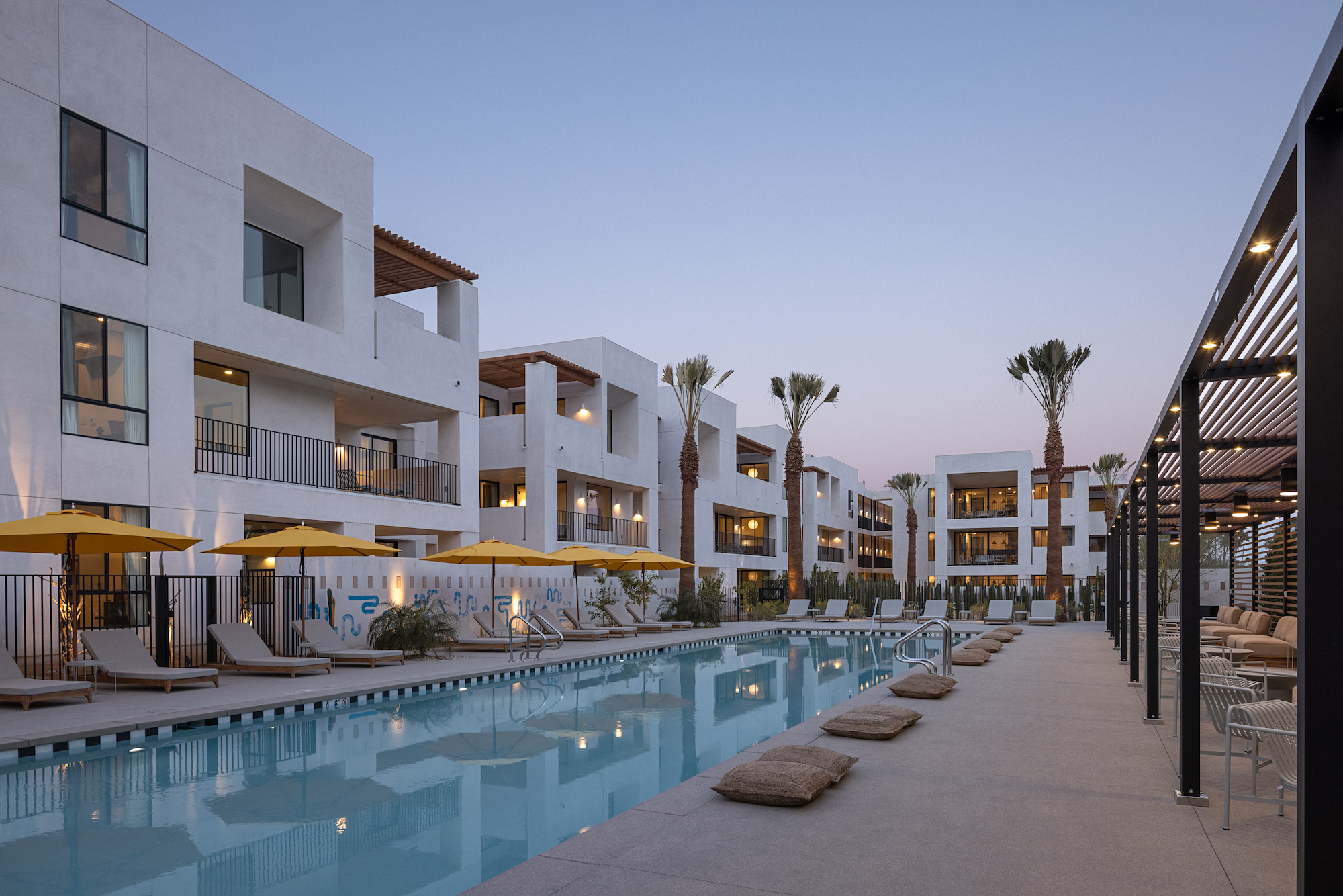 The pool at Drift Palm Springs surrounded by palm trees and loungers and yellow umbrellas