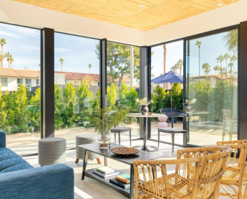 A room with a blue couch and floor to ceiling glass windows that show palm trees outside