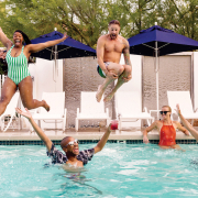 A Black woman and white man jump into a pool where a white woman and Black man are floating