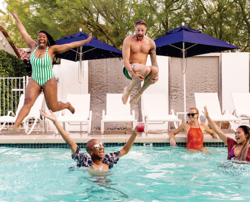 A Black woman and white man jump into a pool where a white woman and Black man are floating