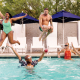 A Black woman and white man jump into a pool where a white woman and Black man are floating