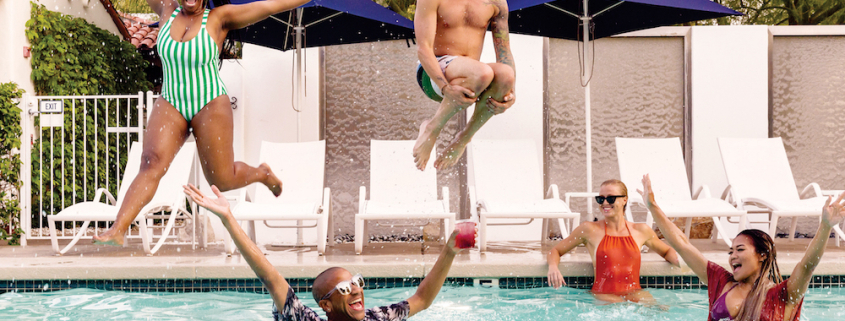 A Black woman and white man jump into a pool where a white woman and Black man are floating