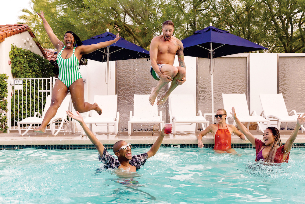 A Black woman and white man jump into a pool where a white woman and Black man are floating