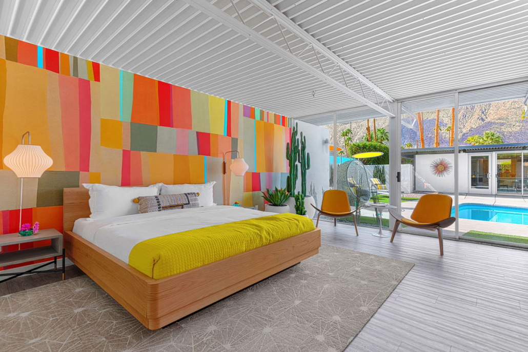 A colorful bedroom at Limon Palm Springs with patterned wallpaper and a bed with a yellow blanket
