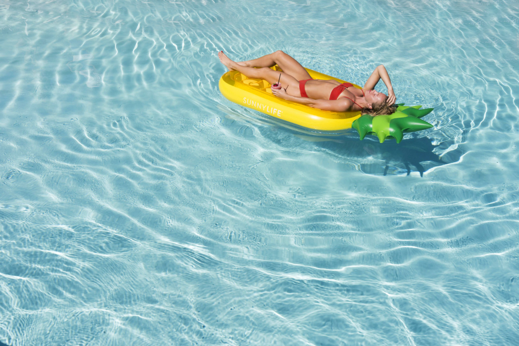 A woman floats on a pool raft shaped like a pineapple