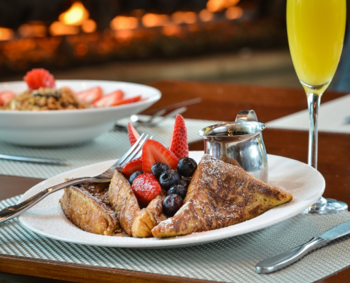 A white plate with French toast and berries on top of it with a mimosa in a glass next to it served at Escena