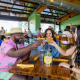 A Black man, a white woman, and a Hispanic woman hold their glasses up to cheers at a table