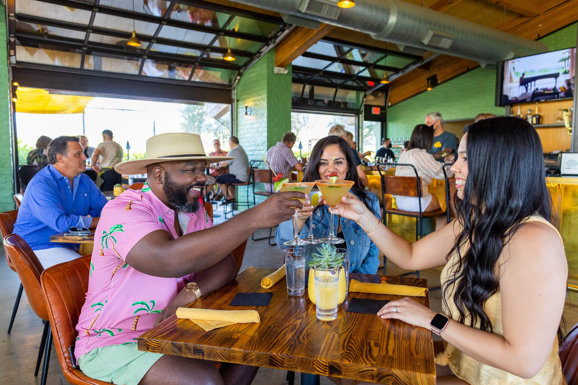 A Black man, a white woman, and a Hispanic woman hold their glasses up to cheers at a table