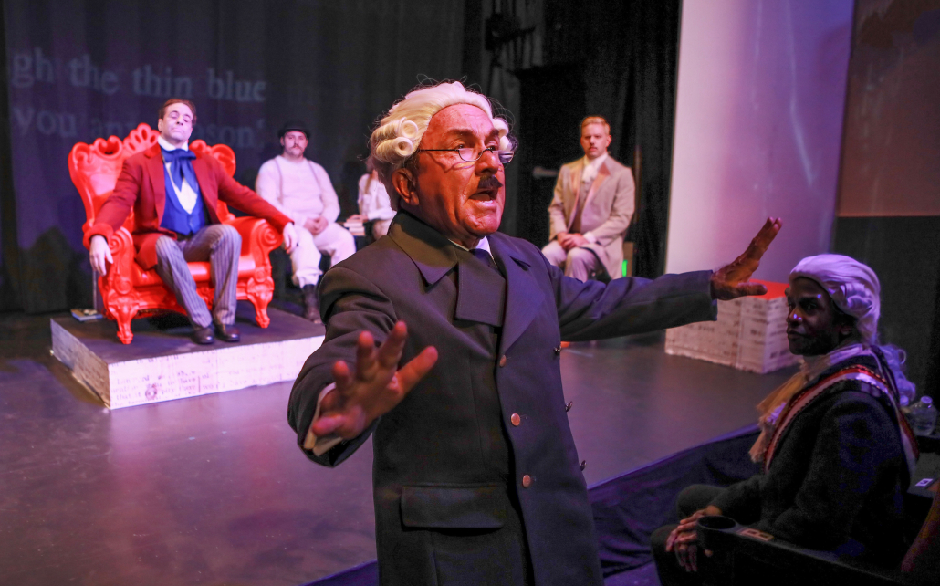 A man with a white wig and black mustache stands with his arms out during a performance of "Gross Indecency: The Three Trials of Oscar Wilde" performed at The Bent in Palm Springs, California