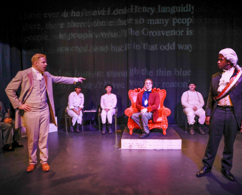 A white man points at a Black man while on stage performing "Gross Indecency" in Palm Springs