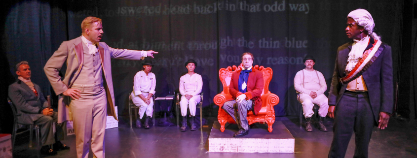 A white man points at a Black man while on stage performing "Gross Indecency" in Palm Springs