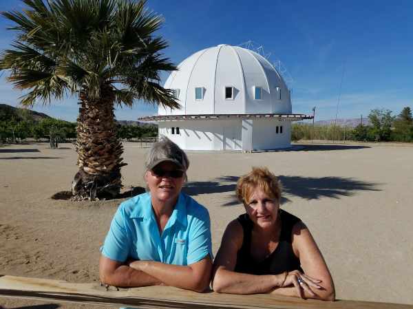 The white domed Integratron in Landers, California, with two women in front of it and a palm tree