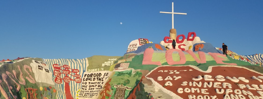 Paint on a rock and a giant cross on the top of Salvation Mountain