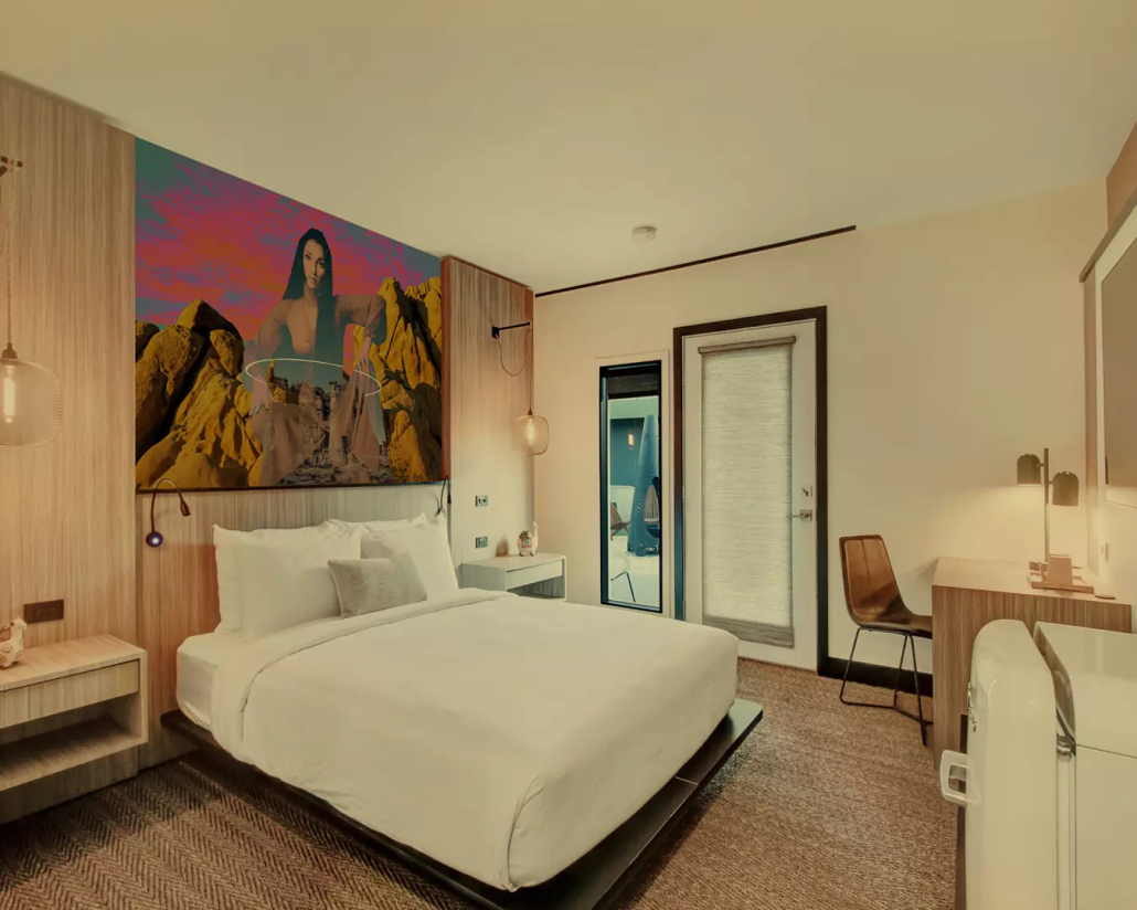A room at Mahala Hotel in Palm Springs, California, with a large art print of Cher on the wall above a bed with white linens