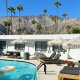 The pool at Jazz Hotel surrounded by fringed umbrellas and lounge chairs with a white ring float in the water and palms and San Jacinto Mountains in the background