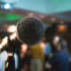 A microphone and stand on a stage with lights and people in the background