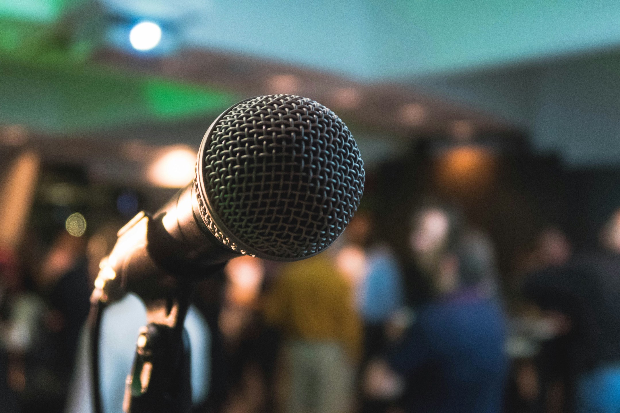 A microphone and stand on a stage with lights and people in the background