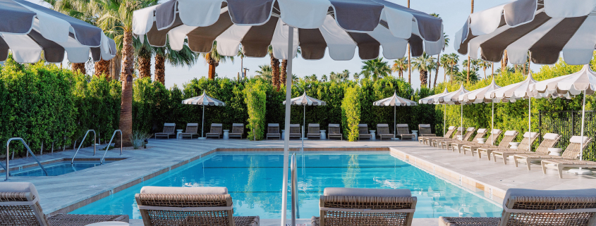 Four lounge chairs and striped umbrellas in front of the pool at Azure Sky Resort in Palm Springs, California