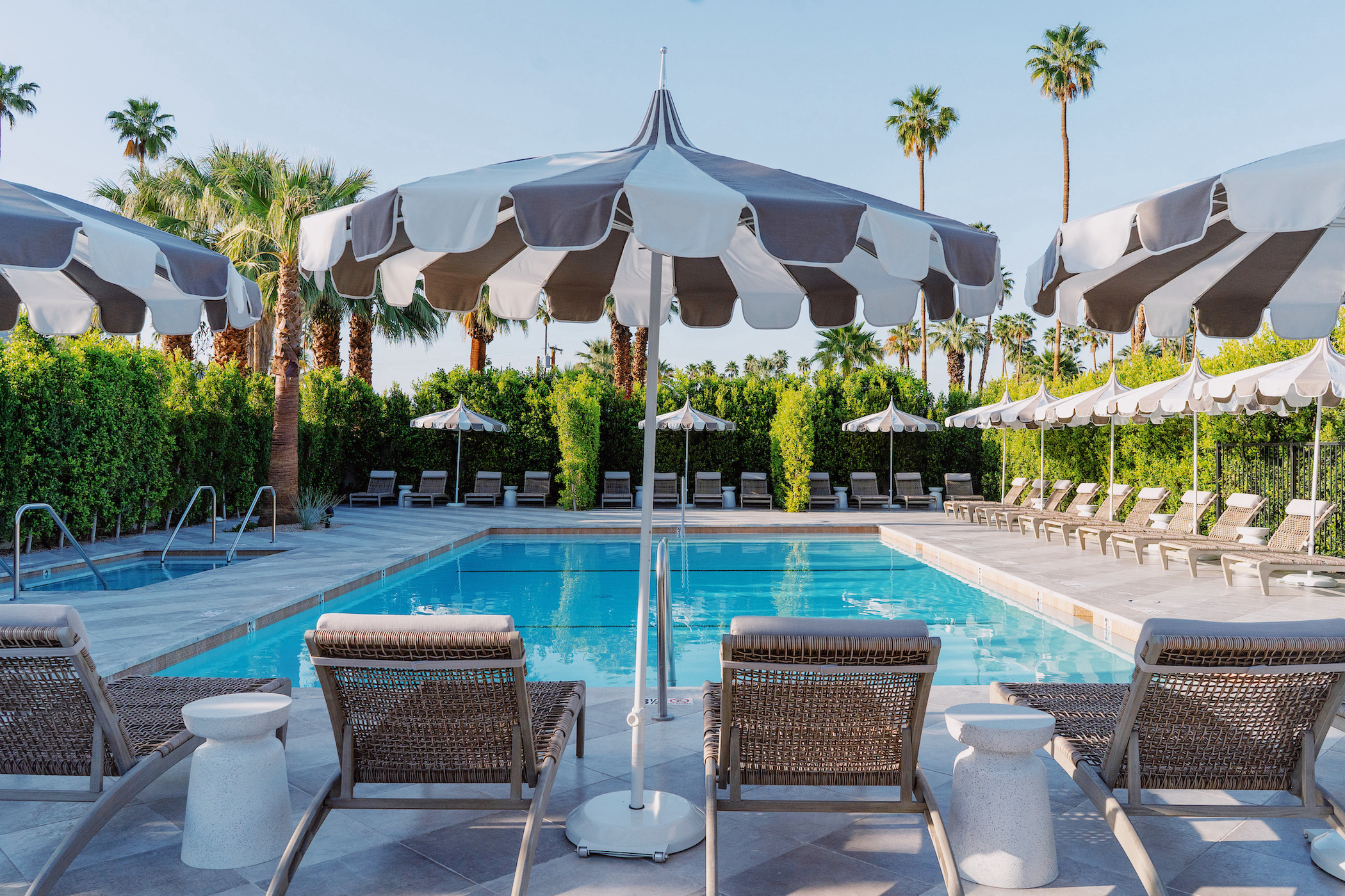 Four lounge chairs and striped umbrellas in front of the pool at Azure Sky Resort in Palm Springs, California