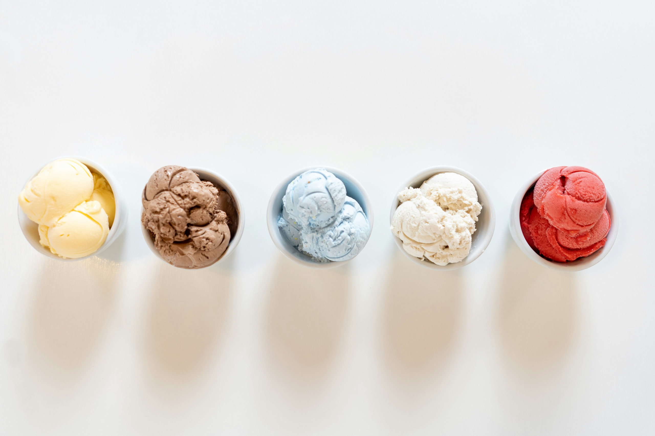 Five bowls of colorful ice cream lined up in white bowls