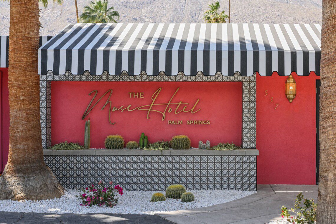 The front of The Muse Hotel Palm Springs is painted pink with a black and white striped awning